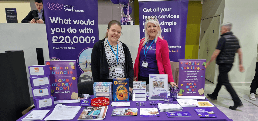 two people standing next to a table with a purple table cloth at a business expo