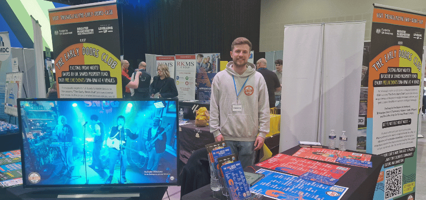 Image shows exhibitor smiling behind his expo stand at Wigan Business Expo
