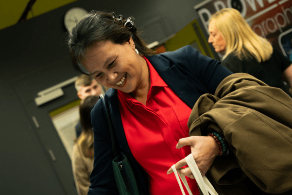 Visitor smiling while collecting a bag during Wigan Business Expo, with other attendees in the background.