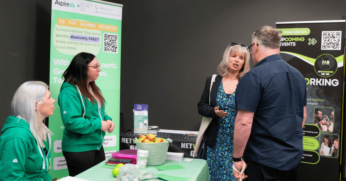 Two representatives from Aspire speak with a visitor at their exhibition stand, with branded banners and promotional materials visible.