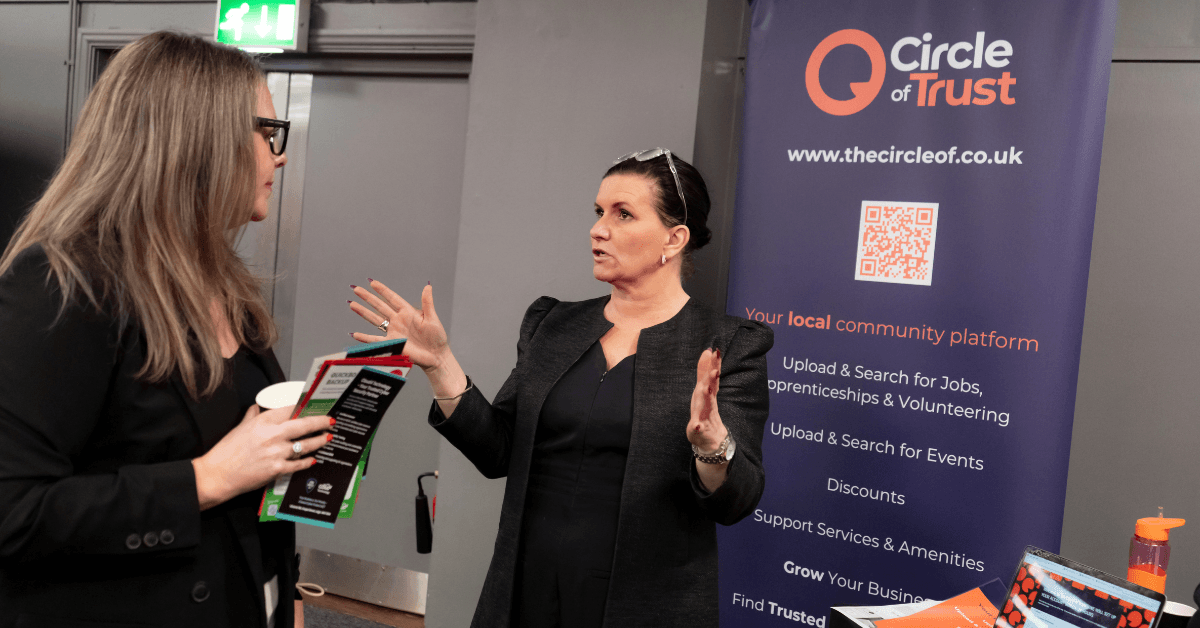 A woman speaks with an exhibitor at the Circle of Trust stand, with the company’s branded banner and community platform information visible behind them.